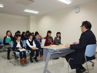 子供数人と保護者が、机を挟んで男の人と話をしている写真。
