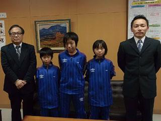 右から、スーツを着た男性と、3人の青いユニフォームを着た生徒と、スーツを着た男性が並んでいる写真