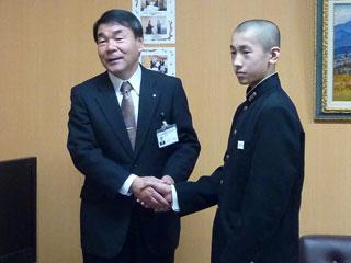 右から、黒い制服を着た男子生徒と、スーツを着た男性が握手をしている写真