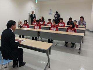 白壁に囲まれた室内で赤いジャケットを着た「岩見沢日の出イーグル」の子どもたちと市長が机向かいに対談している写真