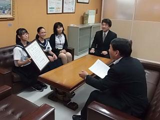 賞状を掲げてを教育長に見せる女子生徒たちの写真