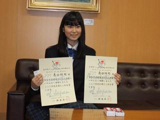 黒い制服を着た女子生徒が両手に賞状を持っている写真