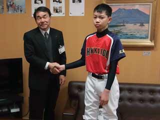 右から、赤と青のユニフォームを着た男子生徒と、スーツを着た男性が並んで握手している写真
