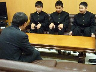 スーツを着た男性と机を挟んで、3人の制服を着た男子生徒が座っている写真