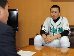坊主頭のユニホームを着た少年とスーツ姿の男性と対面で座っている写真