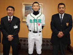 真ん中にユニフォームを着た少年とスーツを着た男性2人とともに並んでいる写真