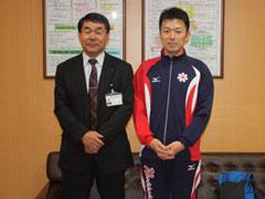 応接室で、ジャージ姿の男子学生と男性が立ち並んでいる記念写真
