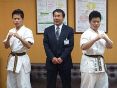 スーツ姿の男性を挟んで柔道着を着た選手二人がポーズをとっている写真