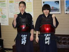 応接室のソファーの前で、剣道着を着た男女1名ずつの学生が、片手を握りしめてガッツポーズをしている写真