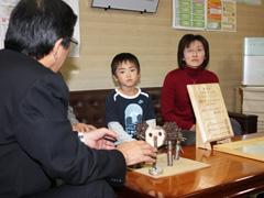 作品が置かれた机の周りに座り話す児童と女性の写真