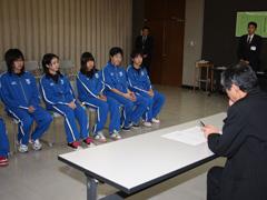男性の前に座る青いジャージを着た女学生たちの写真