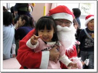 サンタクロースに抱きかかえられ、笑顔でピースサインする女の子の写真