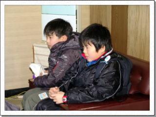 応接室の1人用ソファーに2人で詰めて座る男子児童の写真