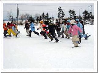 白い雪景色の中でスノーシューを履き一斉に走る複数の児童たちの写真