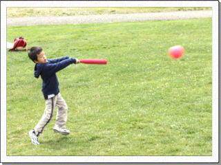 公園の芝生でバットをフルスイングしてボールを打った児童の写真