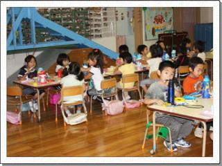 幼稚園で机に向かい、お弁当を食べる子供たちの写真