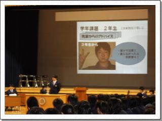 大型スクリーンに3年生からのメッセージが映し出され、その前の演台で男子生徒が話をしている写真