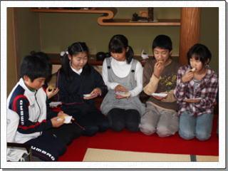 正座し懐紙を手に緊張した様子で和菓子を口に運ぶ6名の児童たちの写真