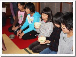 5人の女子児童が正座して並び、中央の2人が手にした茶碗を見つめている写真