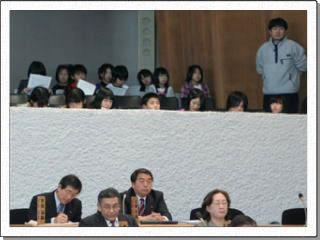 議席の後ろの傍聴席に横に並んで座っている生徒たちと引率の先生の様子の写真