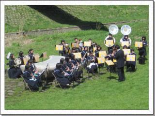 緑の芝生が生い茂った公園でスーザフォンやフルートなど、それぞれの楽器で演奏をする栗沢中学校吹奏楽部の写真