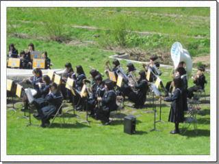 緑の芝生が生い茂った広い公園で演奏する栗沢中学校吹奏楽部の生徒たちを横から写した写真