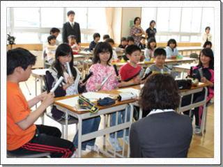 男女6名の児童が机に座りトーンチャイムを手に笑顔で教大生の話を聞いている写真