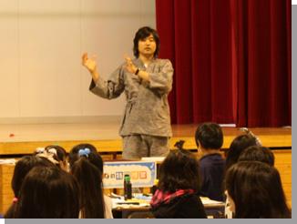 グレーの作務衣を着た武田双雲さんが、両手で表現しながら児童に向かい話をしている様子の写真