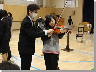 音楽コースの学生に教わりながらバイオリンを演奏している生徒の写真