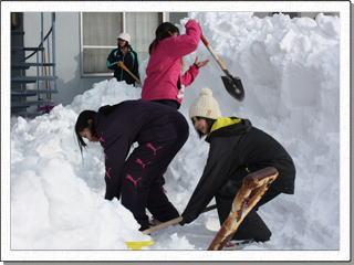 玄関前に高く積もった雪とスコップを使って除雪している生徒達の写真
