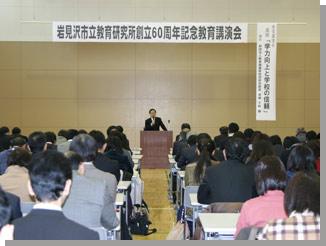 講演会の名称とお題の書かれた看板が吊られている会場で講演をする講師の寺崎千秋さんとそれを聞く参加者の方々の写真