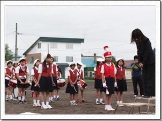 赤いベストを着て白いベレー帽をかぶった児童たちが校庭に整列している写真