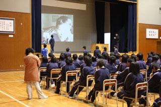 明成中学校全校集会で海外研修中の先生と交流している様子の写真