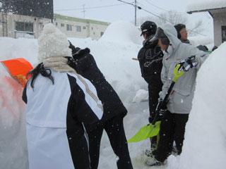 積もった雪をスコップを使って高く積み上げている数人の生徒たちの写真
