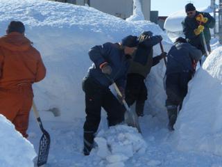 身長以上の高さに積もった雪をスコップを使って掘り起こして道を作っている数人の男性の写真