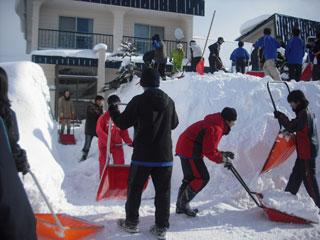 沢山の生徒たちがスコップを使って雪を高く積み上げていて、その脇に平坦な道ができていく様子の写真