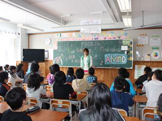 教室で黒板の前に立つ緑色のベストとピンクのズボンの翔太さんを机に座った子どもたちが見つめている写真