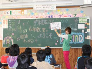 翔太さんが黒板の前で資料を高く上げて指差して説明しているのを、興味津々に見つめている子どもたちの写真