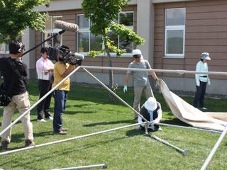 男性がテントのパイプフレームを組み立てている様子を撮っているカメラマンの写真