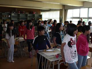 教室で生徒全員が起立し前を向いて話しを聞いている写真