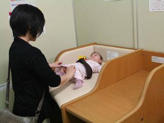 女性が台の上に乳幼児を寝かせ、おむつの交換をしている写真