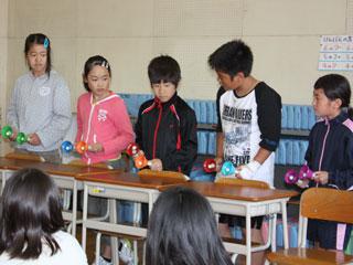 5人の児童が色とりどりのハンドベルを手に横一列に並び演奏をしている写真
