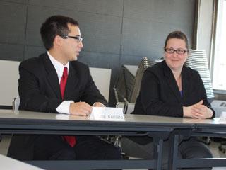 赤いネクタイをしたスーツ姿の男性と、メガネを掛けた女性が顔を合わせて話している様子の写真