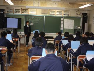 教室の黒板の前に立つ男性と、机に向かい手元のファイルを見ている生徒たちの写真