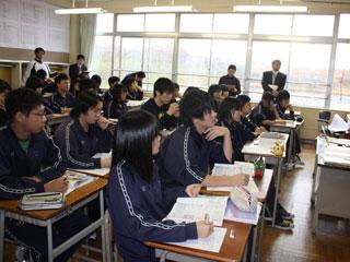教室で数人の大人に囲まれながら、机に向かい真剣に授業を聞くジャージ姿の生徒たちの写真
