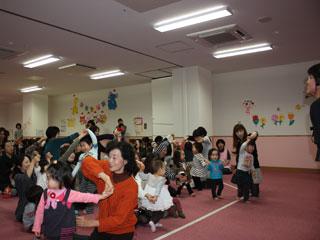 室内で大人に手を取ってもらいながら、楽しそうに踊る子供たちの写真