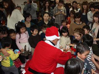 大勢の親子に囲まれ、お菓子を配るサンタクロースの写真