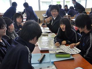 教室の中で机に向かい、グループになって紙を見ながらみんなで話し合っている生徒たちの写真