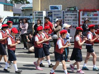 多くの人が見守る中、制服姿の小学生たちがリコーダーを吹きながら通過する写真