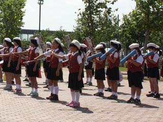 イベントホールの前で整列をして、それぞれの楽器を演奏する小学生たちの写真